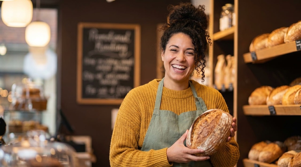 A smiling bakery owner holding a fresh loaf in her shop