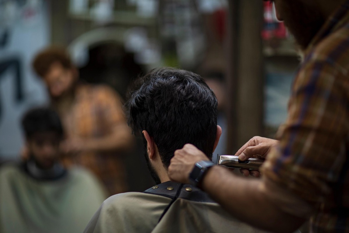 A barber trimming a customer's hair with clippers in a busy shop
