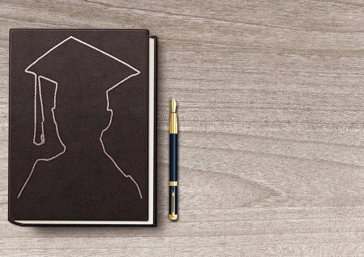 A notebook with a graduation cap drawn on the cover beside a pen