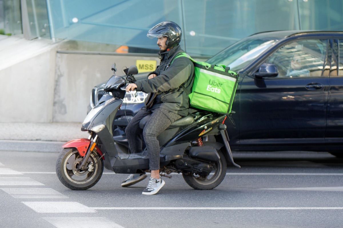 A delivery courier on a scooter with a green delivery box