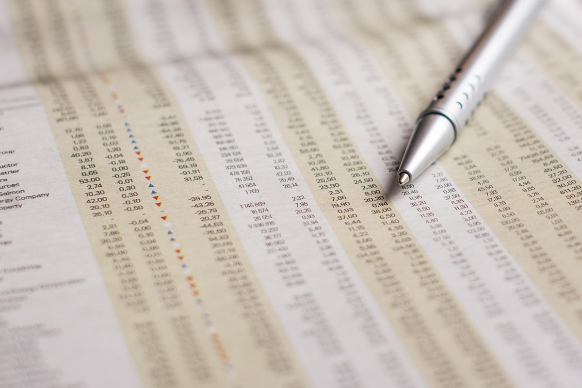 Newspaper stock tables with a pen pointing at a price