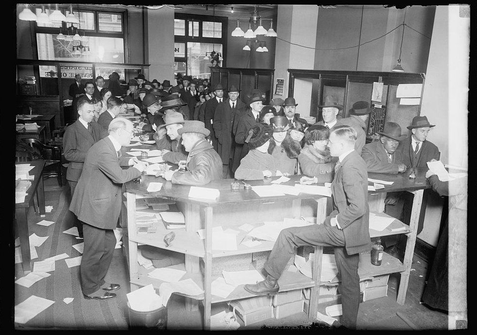 Crowd of filers at tables inside an Internal Revenue office, around 1920